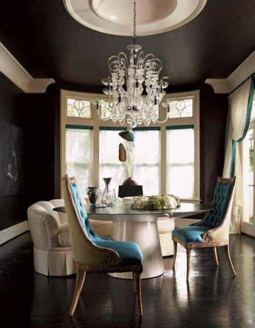 The black hardwood flooring matches with the black walls and ceiling that has a contrasting white circular center dome that supports a white majestic chandelier that perfectly fits the white modern circular glass-top dining table as well as the other white elements that stand out.