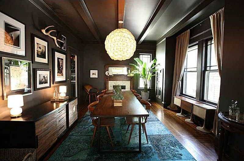 The peculiar spherical pendant light stands out against the black wooden ceiling with exposed wooden beams and the walls that are mostly accented with framed photographs and paintings. the green patterned area underneath the dining set provides a nice dash of color.