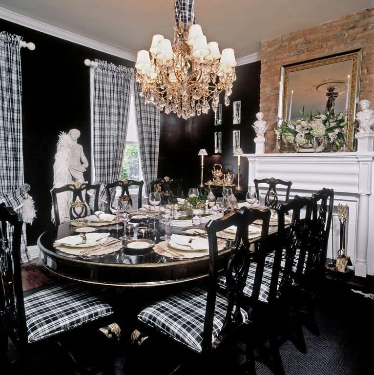 The white mantle of the fireplace stands out against the black walls and the black dining table that is paired with black wooden chairs that have plaid seat cushions matching the curtains flanking the tall windows by the marble statuette.