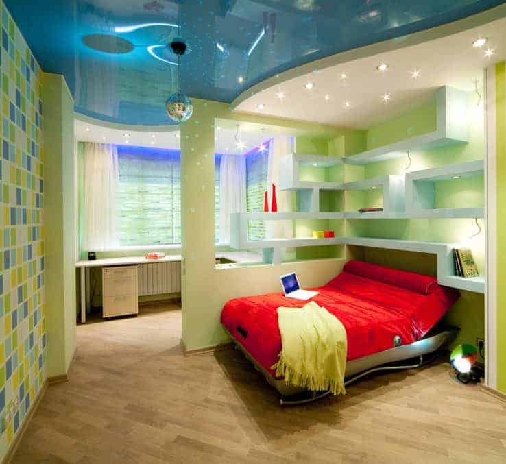 Magnificent bedroom with hardwood flooring and a stylish ceiling mounted with recessed lights and a chrome globe pendant. It has a red bed and an L-shaped desk separated by built-in shelving.