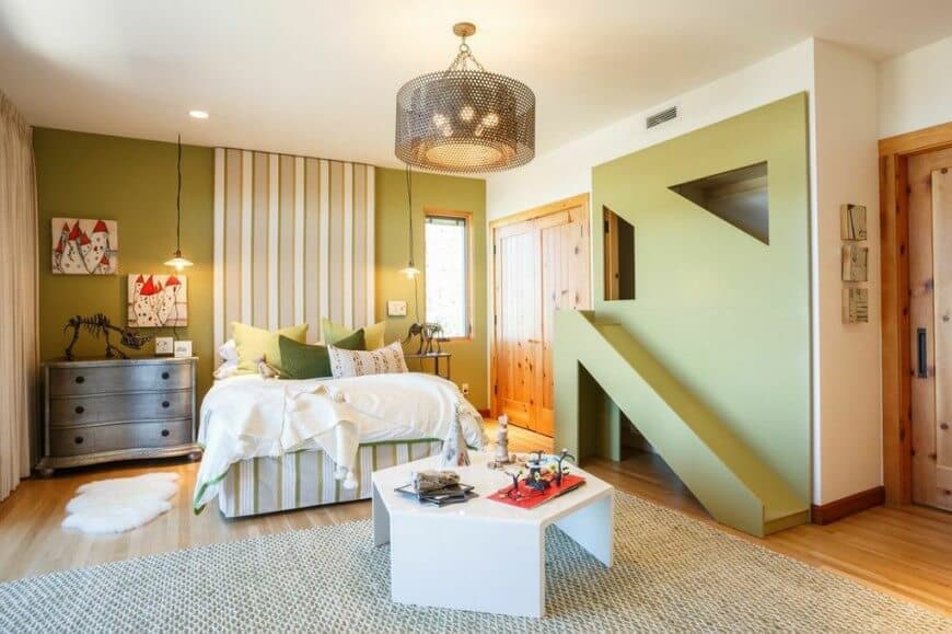 Kids bedroom illuminated by bulb pendants and a perforated drum chandelier that hung over the white sleek table sitting on a non-slip rug. It has a green slide and a striped bed accompanied by wooden drawer chest and nightstand.