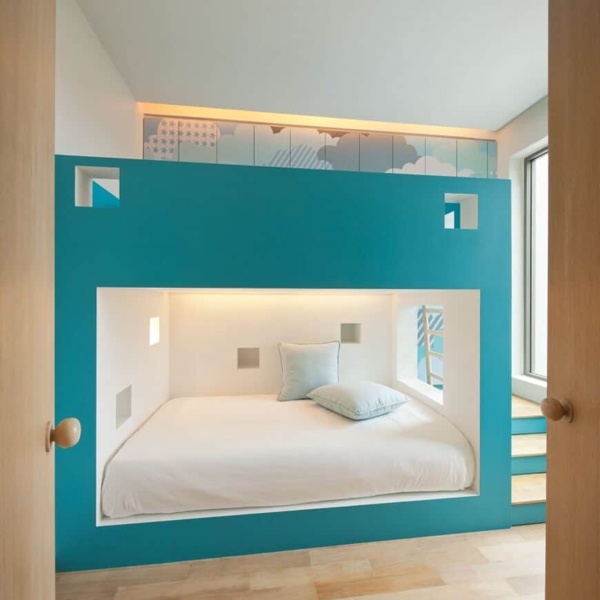 A light wood double door opens to this sleek bedroom featuring a large built-in bunk bed with a teal accent occupying almost the entire space in the room.
