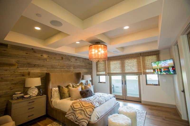 Primary bedroom with a beautiful coffered ceiling along with a rustic wall. The room features hardwood flooring and an elegant bed setup.