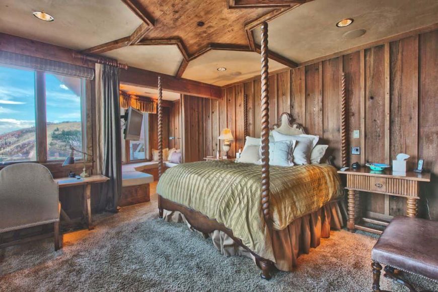 Primary bedroom featuring a stylish rustic-design on the ceiling. It has wooden walls and thick carpet flooring. The room offers a cozy bed and a rustic office desk area, along with a sunroom.