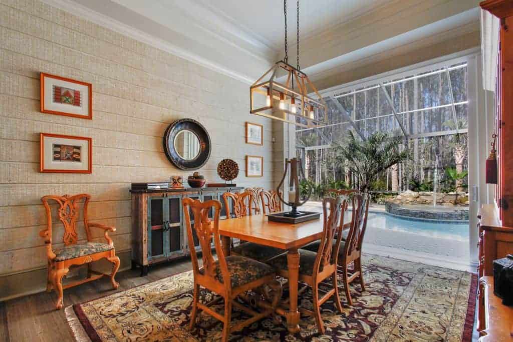 The colorful chic area rug that covers most of the hardwood flooring is a perfect match with the cushions of the wooden dining chairs with the same redwood tone as the wooden rectangular table and the wooden structures and cabinets.