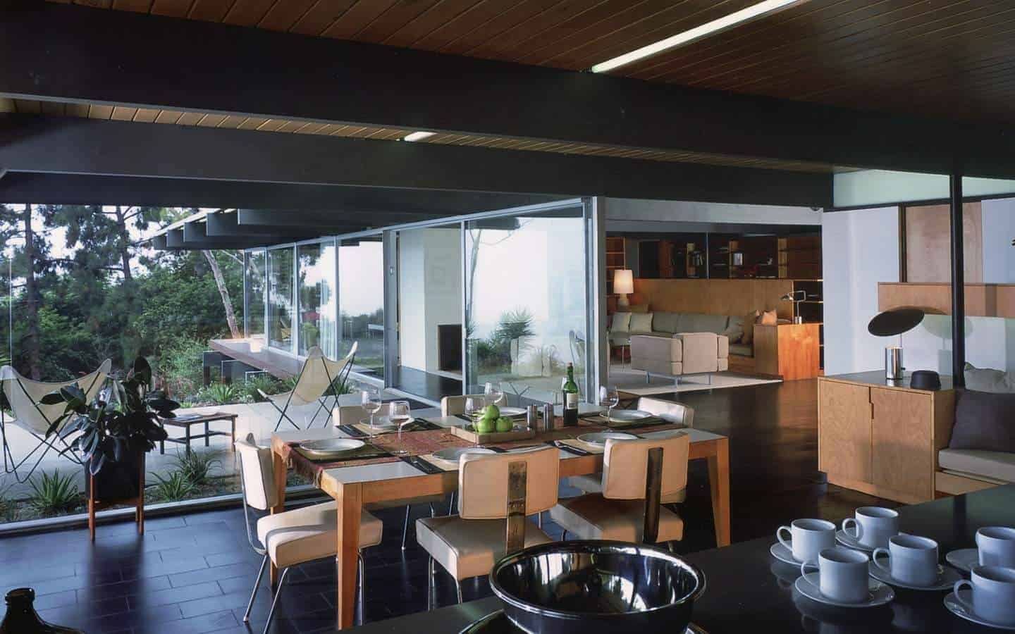This dining room is right beside the kitchen that has the same black flooring tiles and black exposed wooden beams of the brown wooden ceiling with a shiplap design. These black elements make the wooden dining table and its beige chairs stand out.