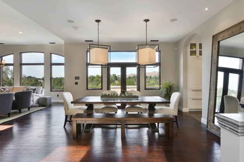 Upon entry of the glass doors of this house, you will see the dining area beside the living room area. The dining set is comprised of a wooden dining table. a wooden bench and four white cushioned chairs. These stand out against the redwood flooring.