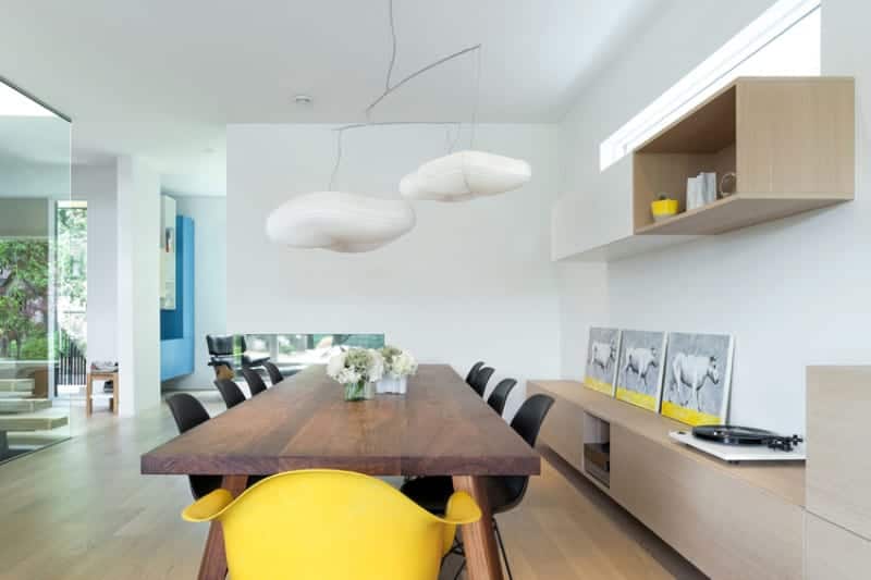 The wooden rectangular dining table is topped with a couple of peculiar white pendant lights that look like clouds. This goes well with the light hues of the walls and ceiling that make it seem like the clouds are floating in the sky over the hardwood flooring matching the cabinets and shelves.