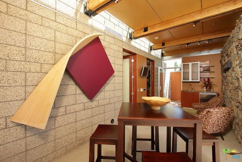 This medium-sized dining room is adorned with a peculiar wooden art piece that is mounted on the gray stone wall by the wooden dining set that has a wooden dining table and benches. This complements the wooden ceiling with exposed beams.