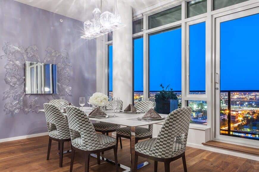 This eclectic dining room is overshadowed by the amazing overlooking view of the city lights. This is featured by the tall glass windows with white frames that blend with the white ceiling and white pendant light over the modern dining set.