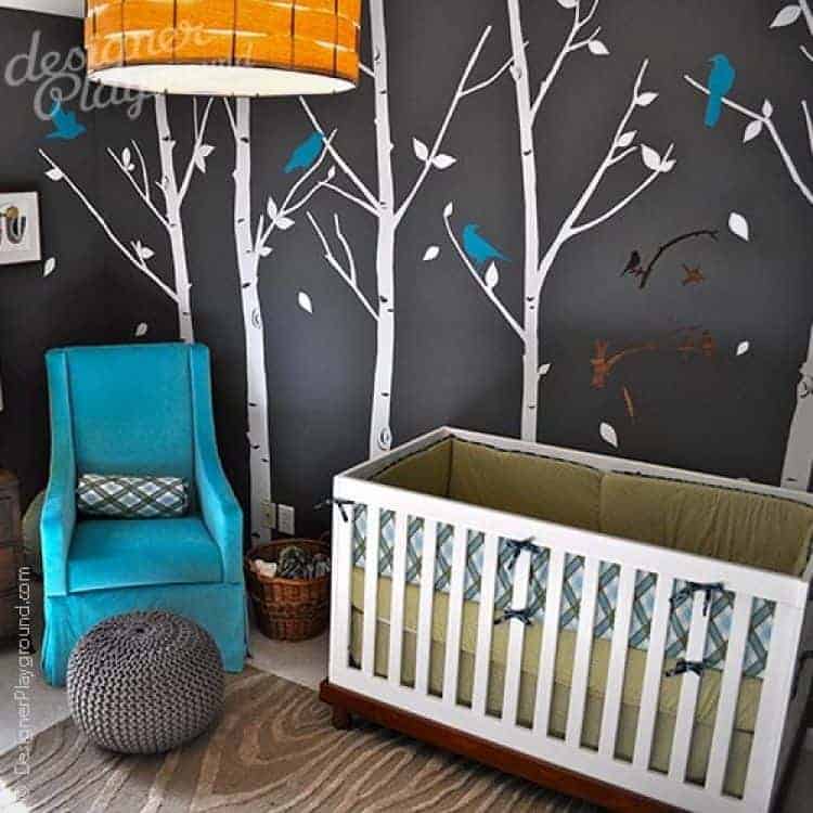 Clad in trees and birds wallpaper, this nursery boasts a white crib and blue skirted armchair paired with a round knitted ottoman on a textured area rug.