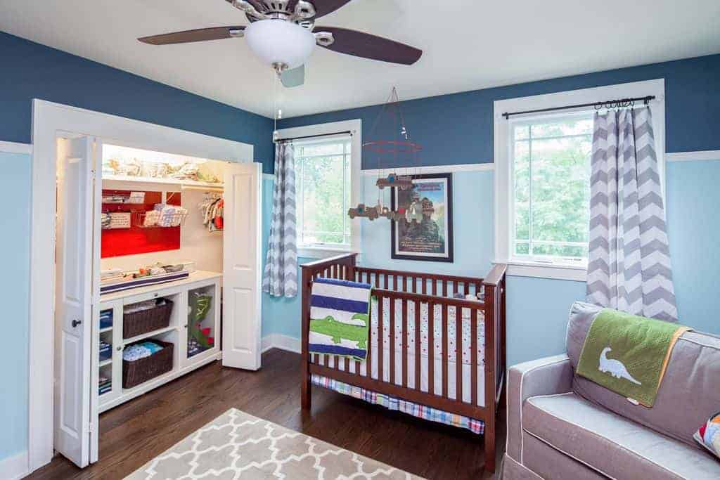 Cool nursery with a wooden crib and gray seat that complements the patterned area rug and chevron draperies. It includes a built-in closet enclosed in folding doors.