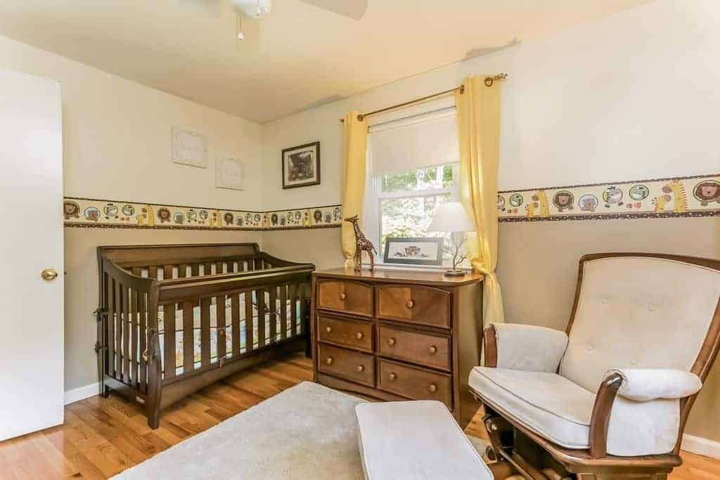 This nursery is furnished with a wooden crib and cabinet along with a cushioned armchair that's paired with a matching ottoman sitting on a gray rug.