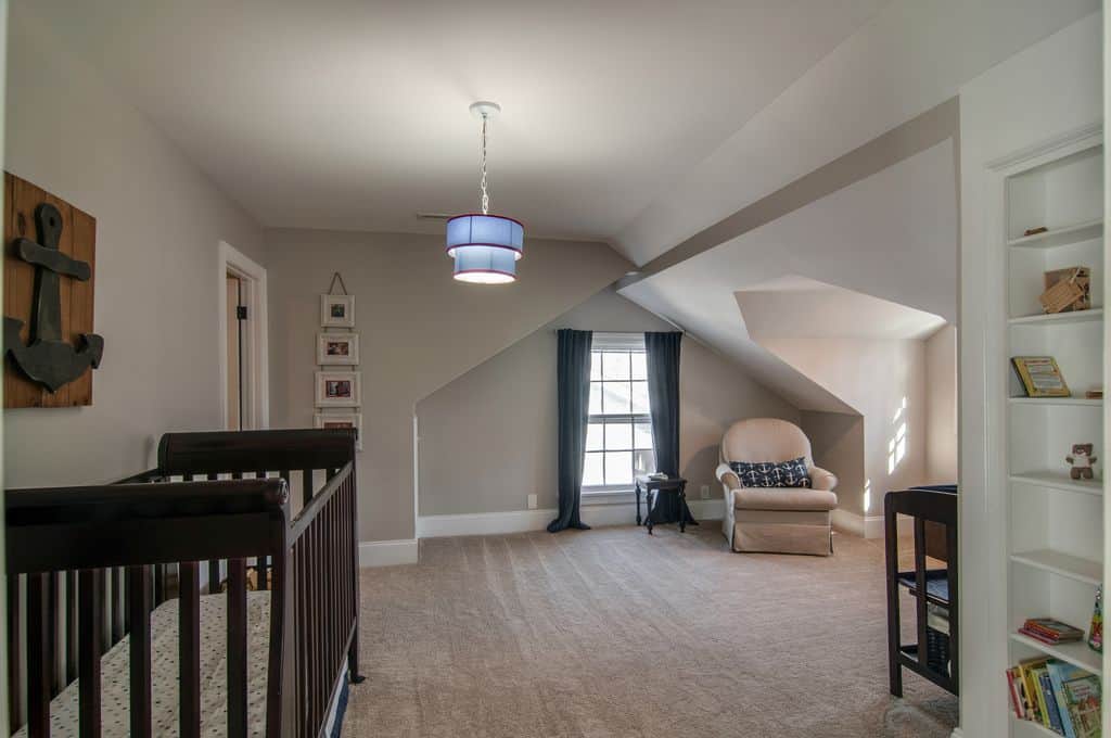 A decorative anchor wall art hangs above the wooden crib in this spacious nursery with a blue two-tier drum pendant and skirted armchair situated underneath the vaulted wall.