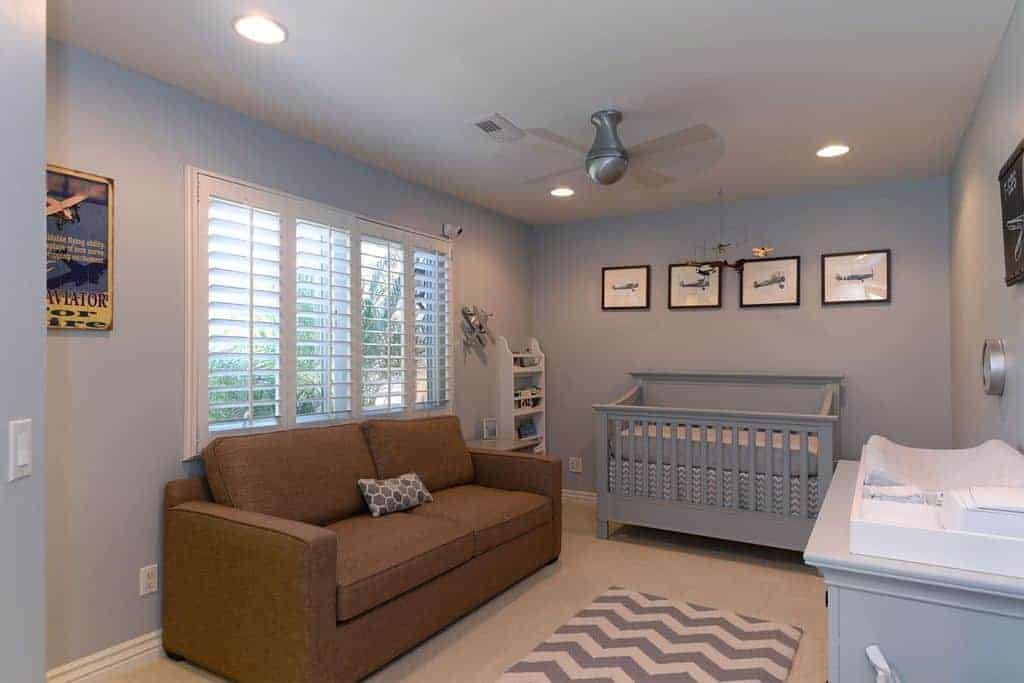 A brown sectional sofa stands out in this gray nursery showcasing a comfy crib and chevron rug that lays on the carpet flooring.