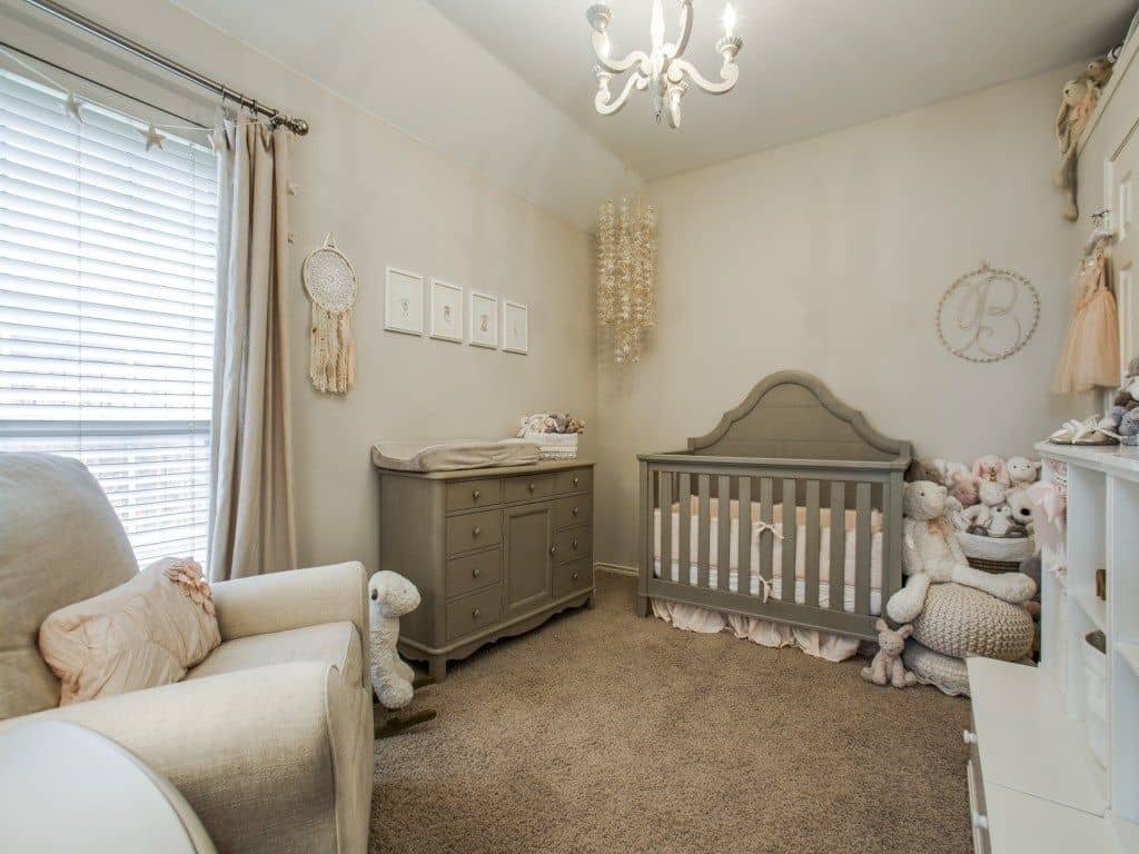 Boho style nursery with a lovely chandelier, a comfy armchair and wooden dresser complementing with the shiplap crib over carpet flooring.