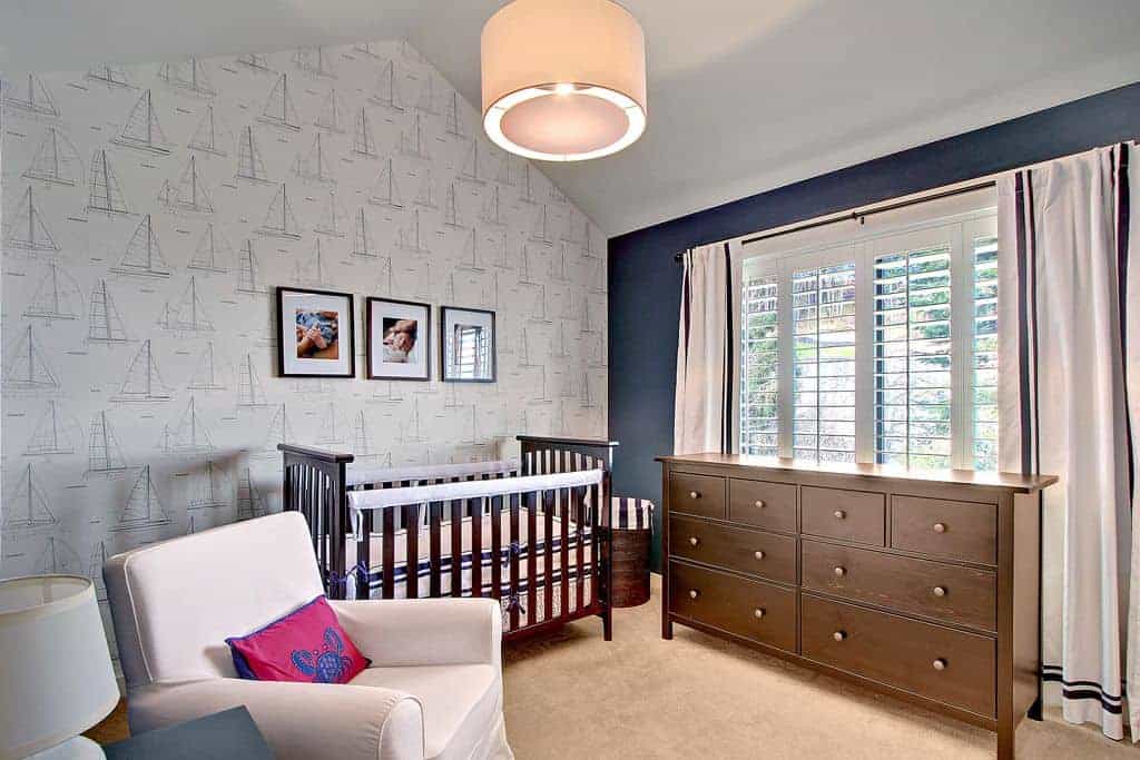 Black framed photos hang over the dark wood crib accompanied by a wooden cabinet and gray skirted armchair that's accented with a pink pillow with crab print.