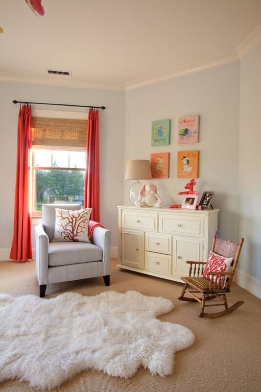 A white faux fur rug lays on the beige carpet flooring in this nursery offering a gray armchair and wooden rocking chair with a cream cabinet in the middle accented by animal wall arts.