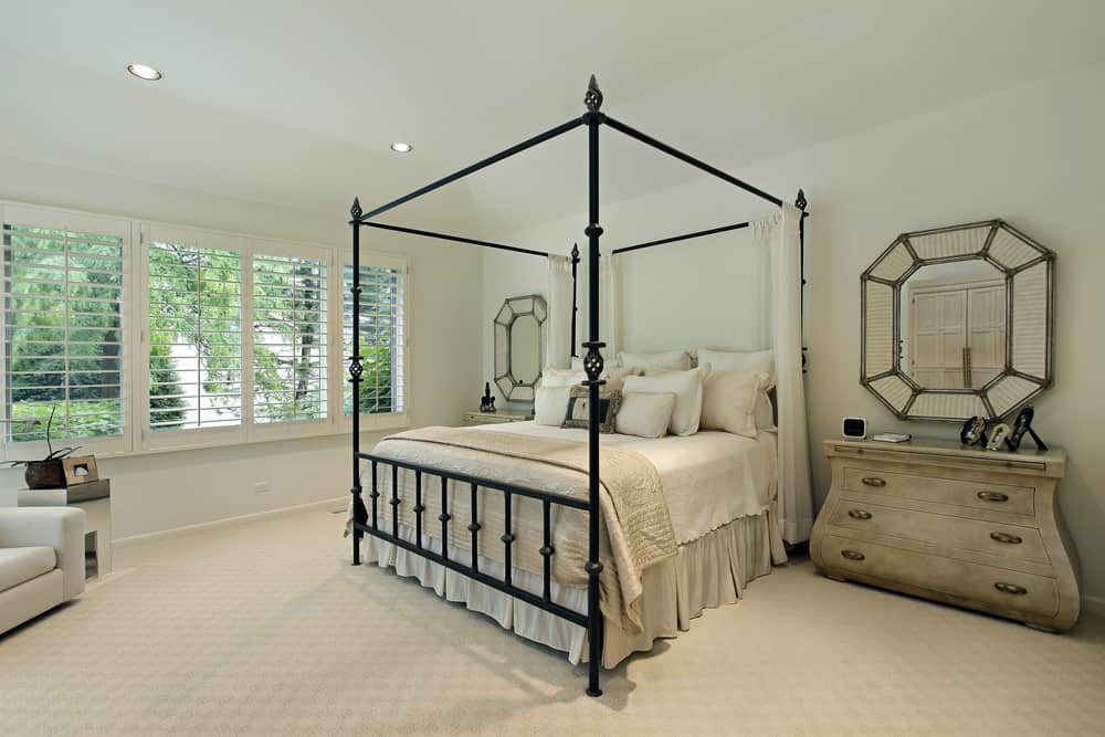 Large Country style primary bedroom featuring classy carpet flooring and white walls. It has a nice bed along with rustic side tables.