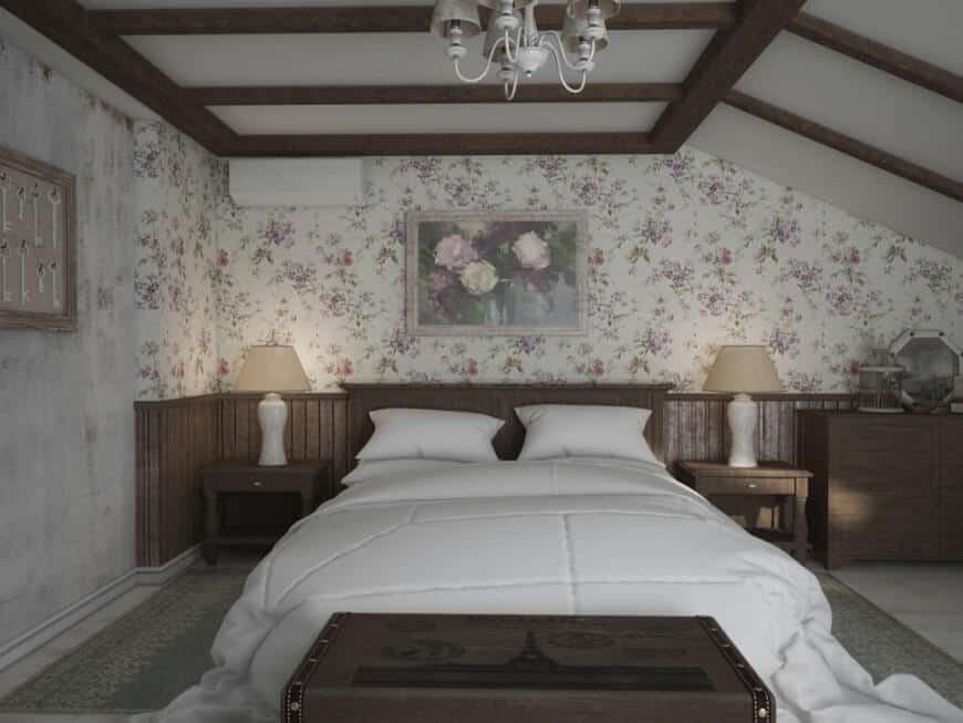 This primary bedroom boasts classy walls and a ceiling with exposed beams. The room offers a white comfy bed along with rustic side tables topped by table lamps.