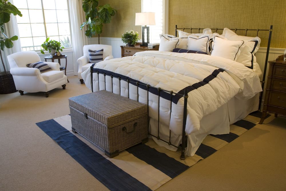 Primary bedroom featuring brown carpeted flooring and brown walls, along with a pair of white seats on the side matching the white bed.