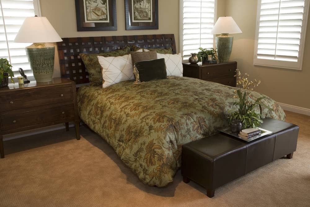 This bedroom offers a classy bed setup lighted by two table lamps set on top of bedside cabinets. The room also has carpet flooring.