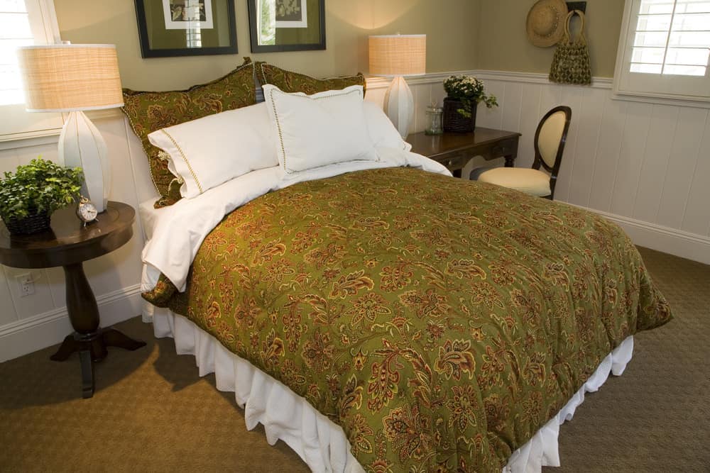A focused look at this primary bedroom's large classy bed lighted by table lamps on both sides. There's a small desk with a chair on the side of the bed.