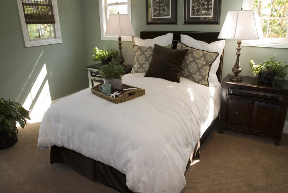 A focused shot at this primary bedroom's double-sized bed surrounded by green walls and is lighted by a pair of table lamps.