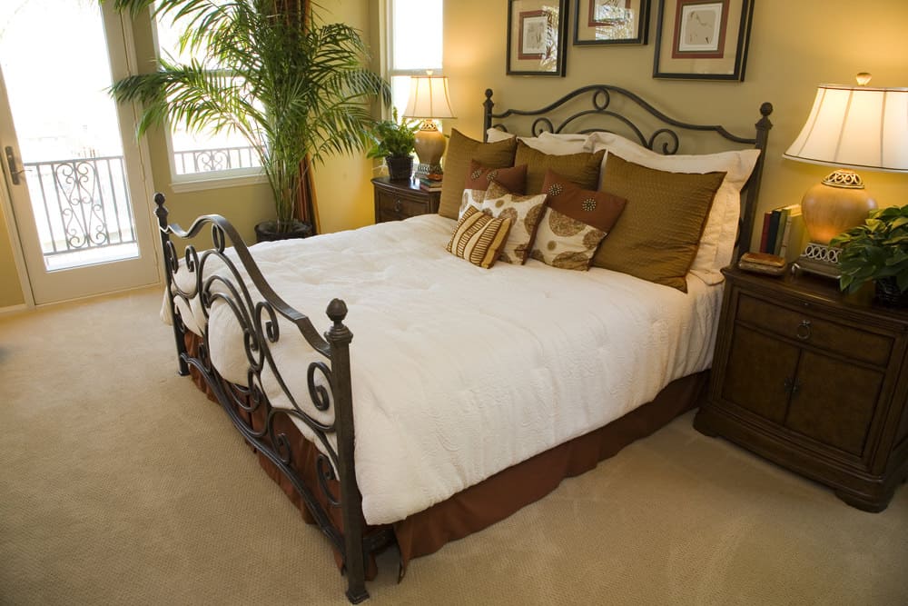 Primary bedroom featuring a classy bed lighted by table lamps on both sides, set on the carpet flooring. The room offers its own balcony area.