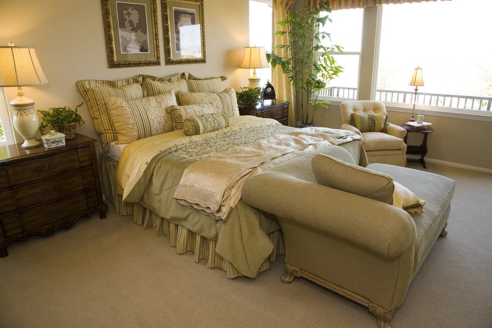 A focused shot at this primary bedroom's large classy bed with a couch at the edge. The bed setup is lighted by a couple of table lamps that look elegant.