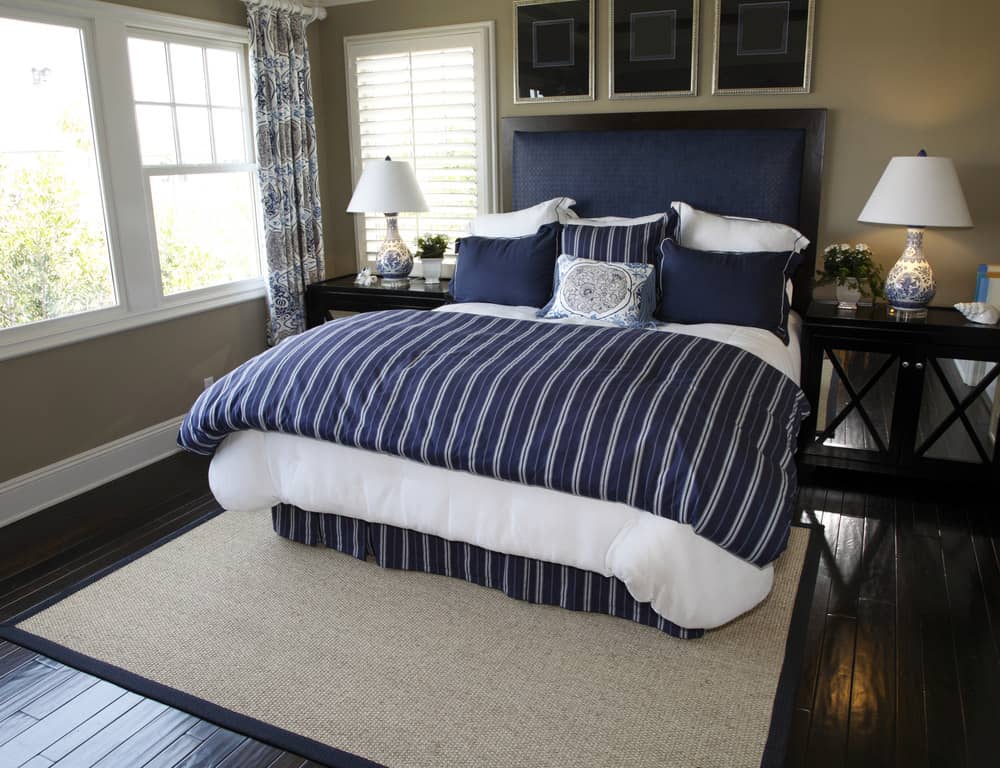 A focused shot at this primary bedroom's navy blue bed setup with a brown area rug on top of the hardwood flooring.