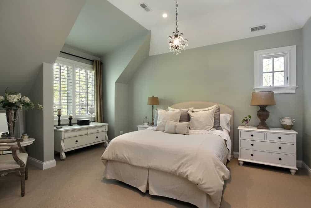 Country style primary bedroom featuring carpet flooring and green walls, along with a tall ceiling. The room offers a nice bed lighted by a fancy pendant light.