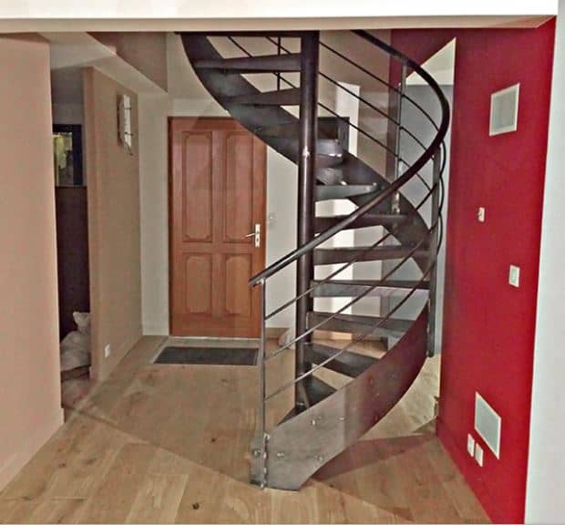The brown wooden door leads into this industrial-style foyer that is dominated by a large metal spiral staircase that solidifies its industrial-style claim. This is paired with hardwood flooring and a red wall that contrasts the fray metallic hue of the stairs.