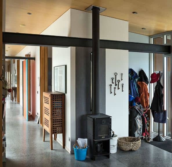 The warm and welcoming demeanor of this industrial-style foyer is due to the freestanding black iron fireplace near the mudroom that is filled with jackets, hats and bags. This pairs well with the gray industrial-style flooring that contrasts the light hue of the walls.