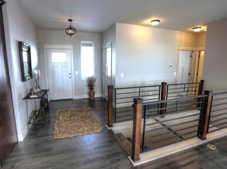 This simple industrial-style foyer has a white wooden door with a glass panel on it matching the window beside it. This door contrasts the gray hardwood flooring that complements the industrial-style semi-flush mount light and the dark iron console table on the side.
