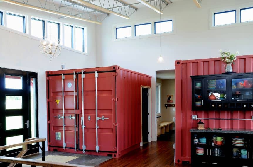 The main door of this industrial-style foyer is a stylish dark wooden door with glass panels matching the side lights. Upon entry, the guest's attention is immediately pulled by the couple of truck containers fitted into the house to be part of the decor and the house as a couple of rooms with doors.