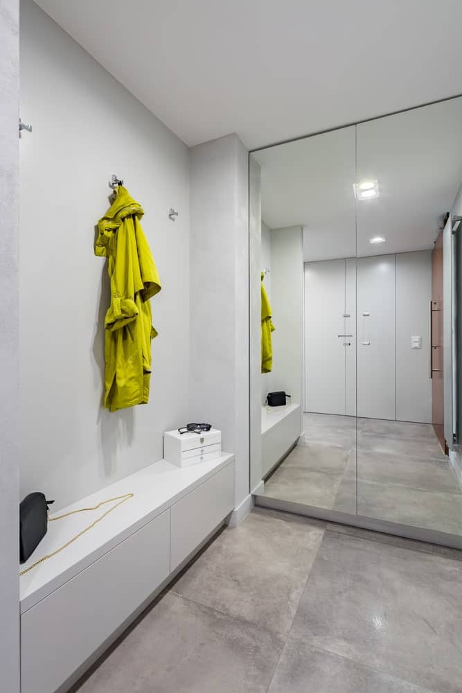 Upon entry of the wooden main door of this foyer, you are welcomed with bright white walls that are augmented by the modern flush-mount light mounted on the white ceiling that is complemented by the industrial-style gray flooring.