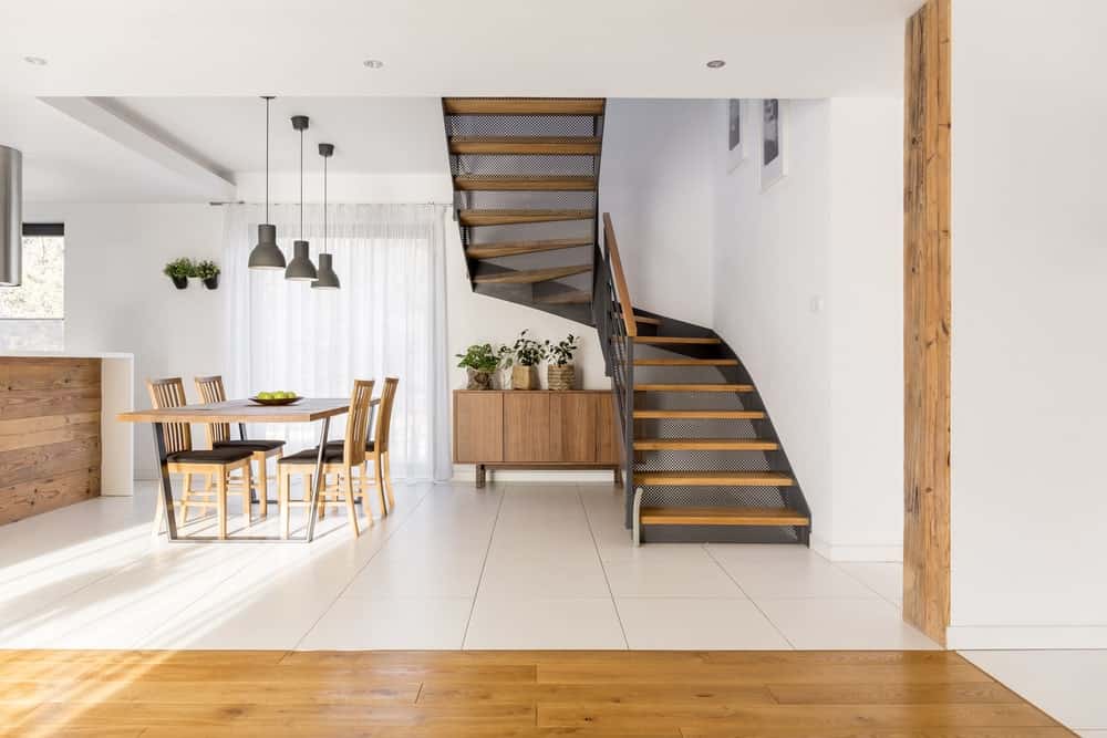 This foyer has a clear view of the dining room by stairs that has the same industrial-style to it as the dining set. There is also a console table against the white walls that pairs well with the flooring tiles. This transitions to hardwood flooring as it nears the foyer.