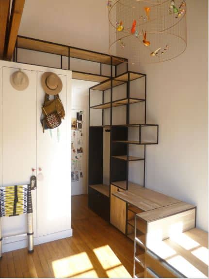 This small foyer is maximized with a large structure made of black iron and wooden shelves. This serves as a mudroom, sitting area, shoe rack, storage area and as a nice accent to the tall white walls that are contrasted by the hardwood flooring.