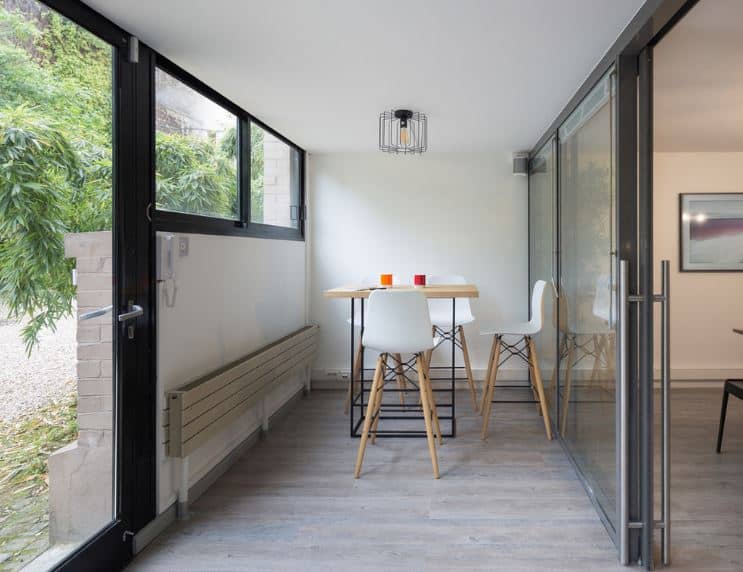 The glass main door leads to this small foyer that has a sitting area with white stools around an industrial-style wood-top table under a caged light bulb from the white ceiling. Along the wall is a folding bench for additional seats of the waiting guests.