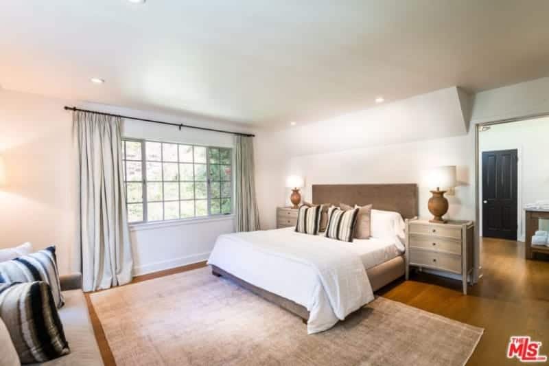 Large primary bedroom featuring hardwood flooring topped by a large area rug. The room has a cozy bed and a comfy couch.