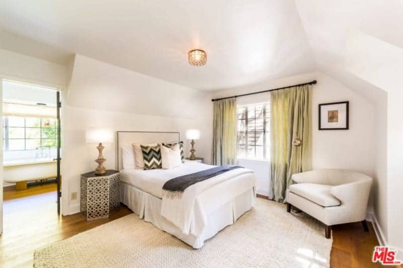 Large primary bedroom featuring hardwood flooring and white walls. The room has a comfy double-sized bed along with its own bathroom featuring a freestanding tub.