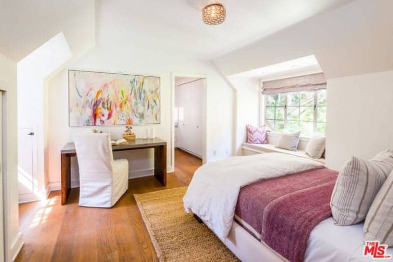 Primary bedroom featuring hardwood floors and white walls. The room has a nice white bed along with a small dining table on the side.