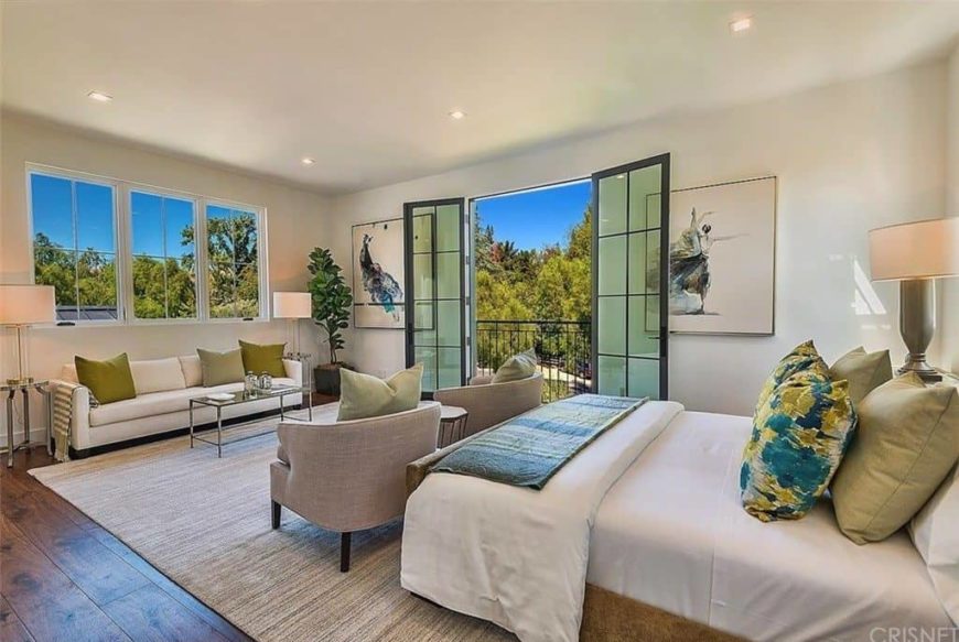 Large primary bedroom featuring hardwood flooring and a regular ceiling. It offers a nice bed along with a white couch near the windows, lighted by two table lamps.