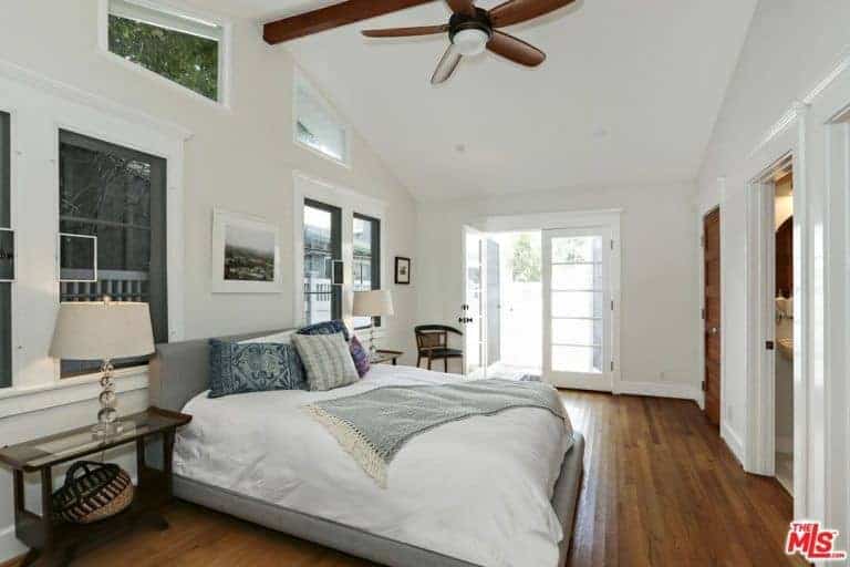 Primary bedroom featuring hardwood flooring and a tall ceiling, along with glass windows. The room offers a large cozy bed and has its own bathroom and closet.