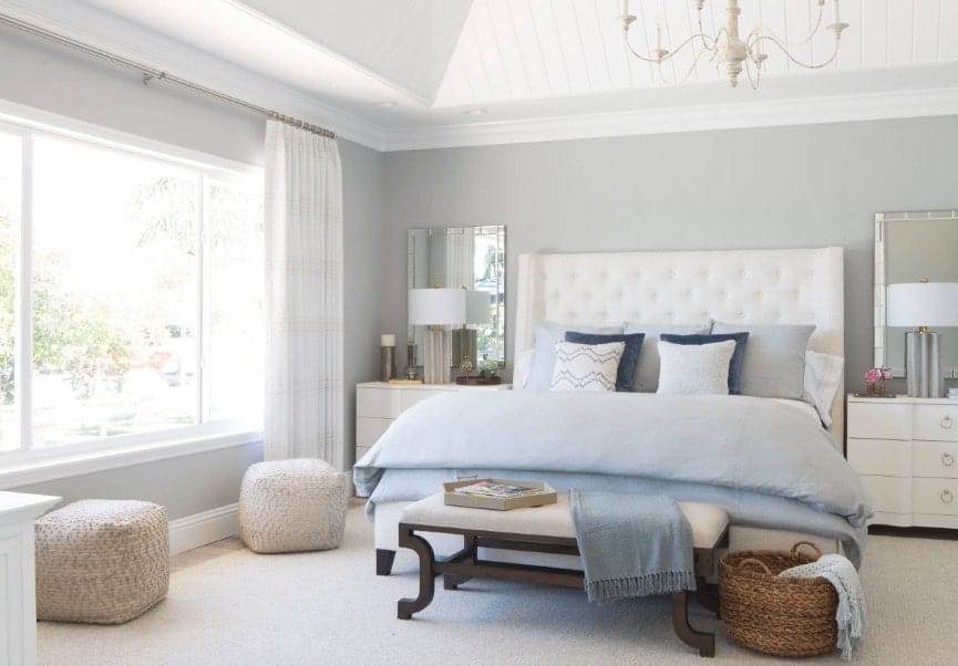 Bright primary bedroom with gray walls and a white ceiling. The room has a large bed and two table lamps, along with a gorgeous chandelier.