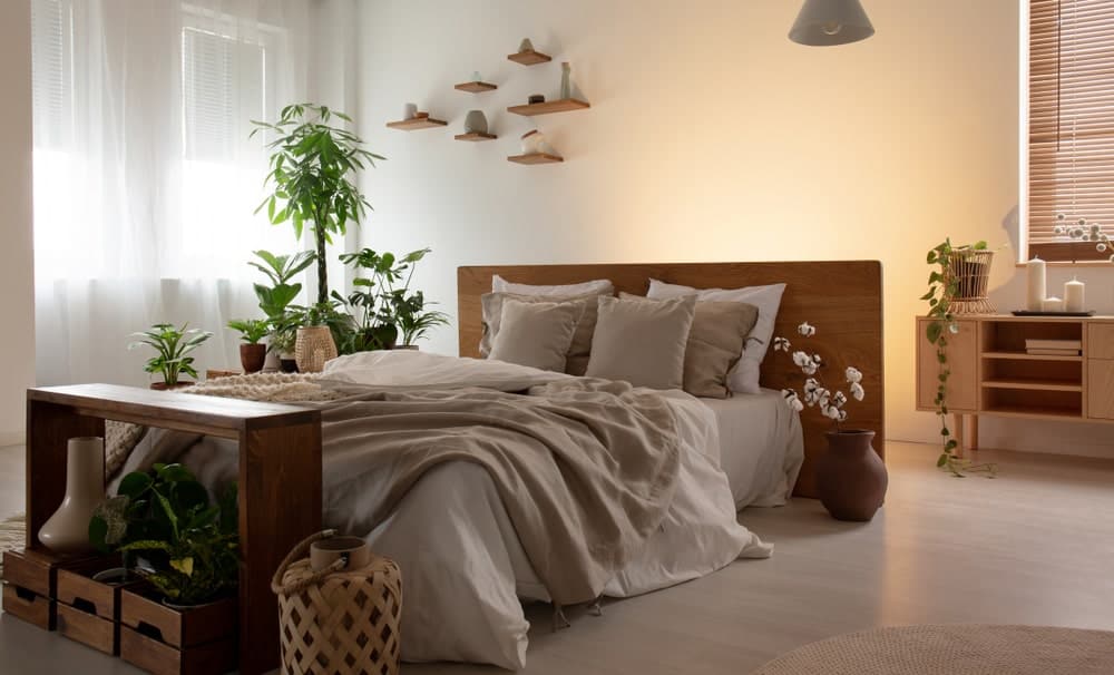 A sleek console table sits behind the wooden bed that's surrounded by potted plants, floating shelves and a bench with storage boxes underneath.