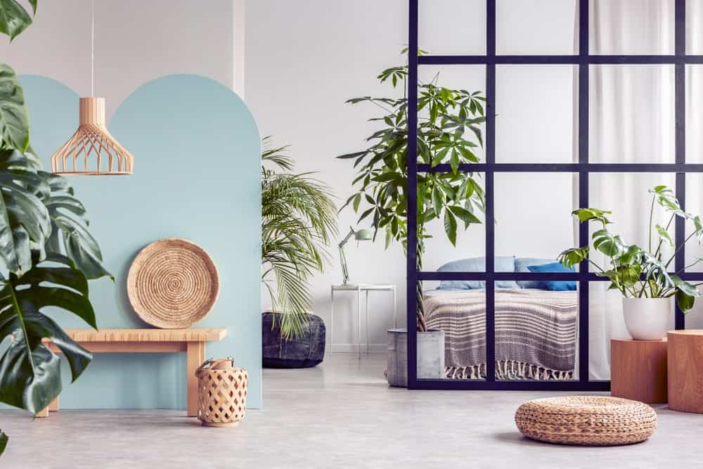 Green potted plants create a refreshing ambiance in this white bedroom with a wooden bench and comfy bed enclosed in a glass panel that's framed in black aluminum grid.