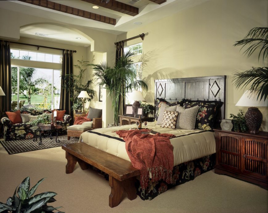 Fresh bedroom offers a beadboard bed with a wooden bench on its end along with a black floral sofa accompanied by a round glass top coffee table and gray lounge chair.