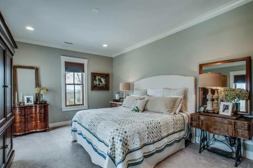 Primary bedroom featuring carpet flooring and gray walls. It has a large comfortable bed lighted by two table lamps on both sides.